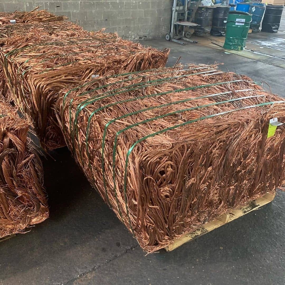 Stacked copper cathodes and coils in an industrial warehouse under cool overhead lighting