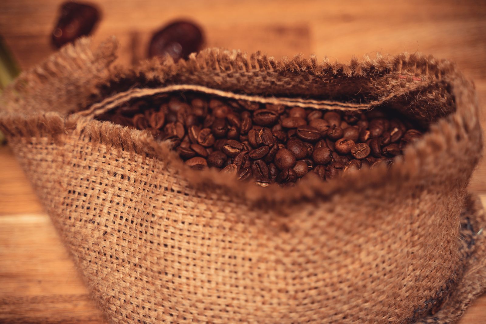 Roasted coffee beans spilling from a burlap sack onto a rustic wooden surface
