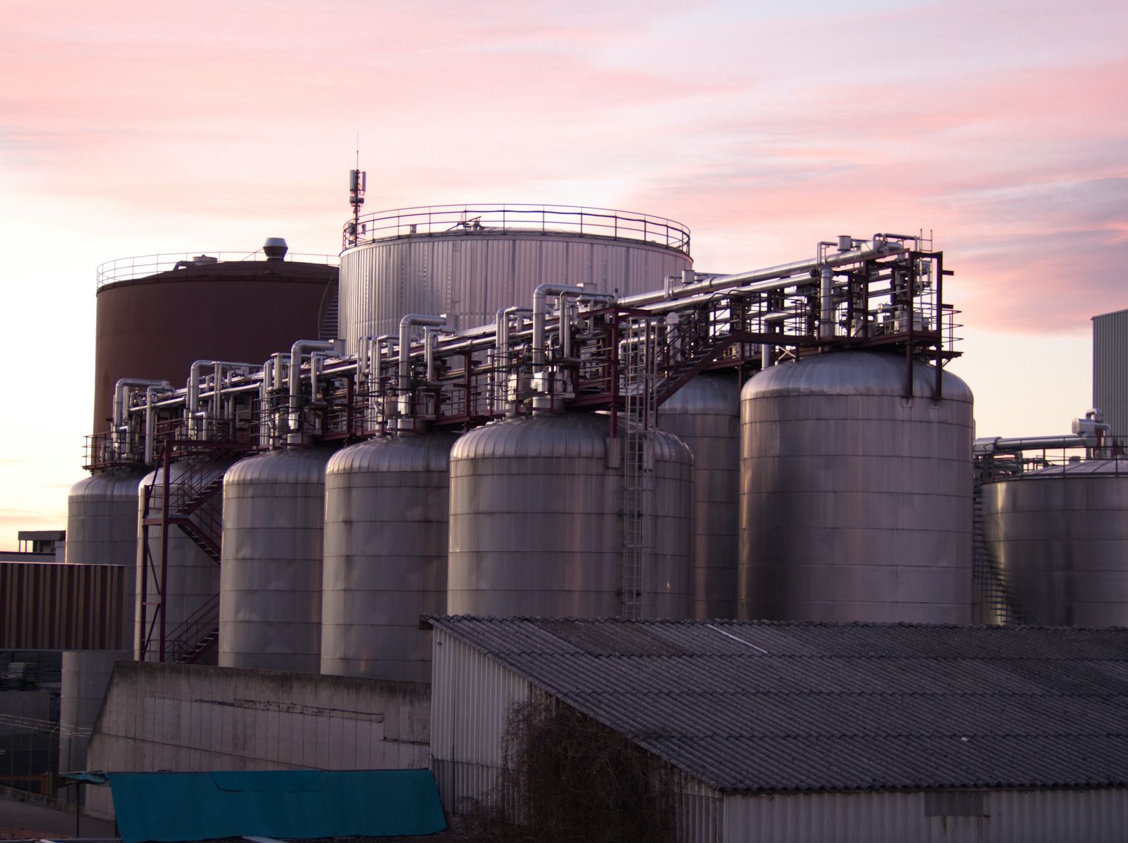 Oil storage tanks and pipelines at sunset with an industrial refinery silhouette