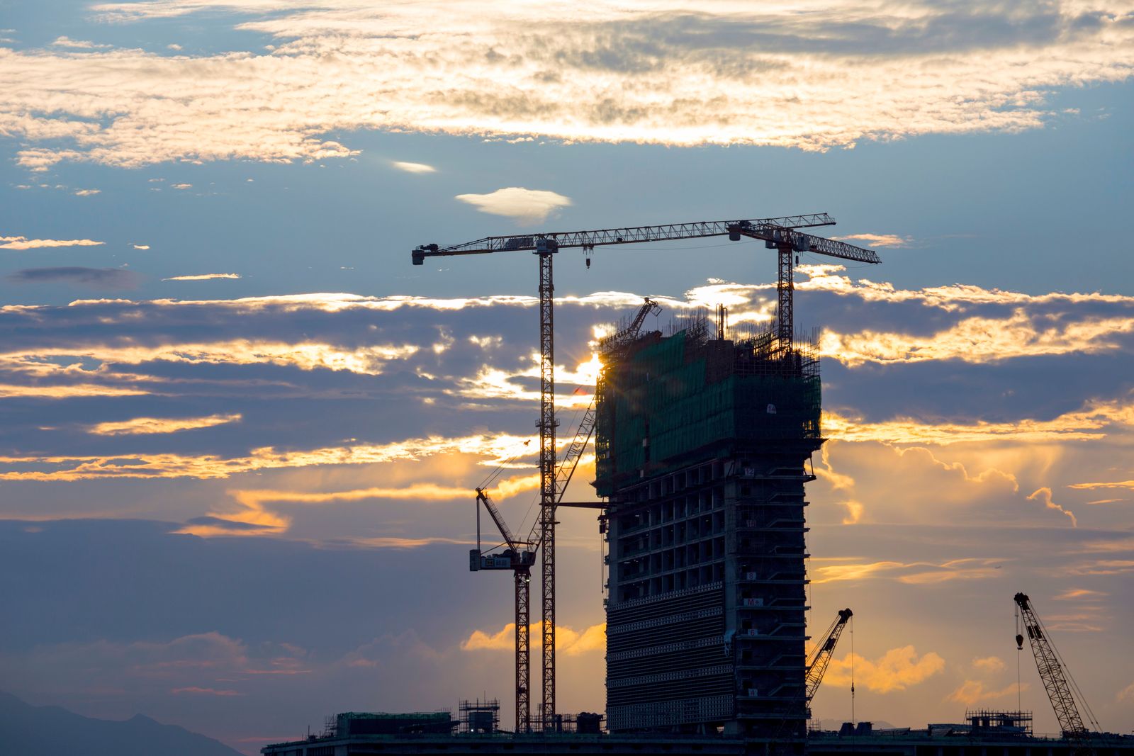 Modern residential development under construction at golden hour, cranes silhouetted against the sky