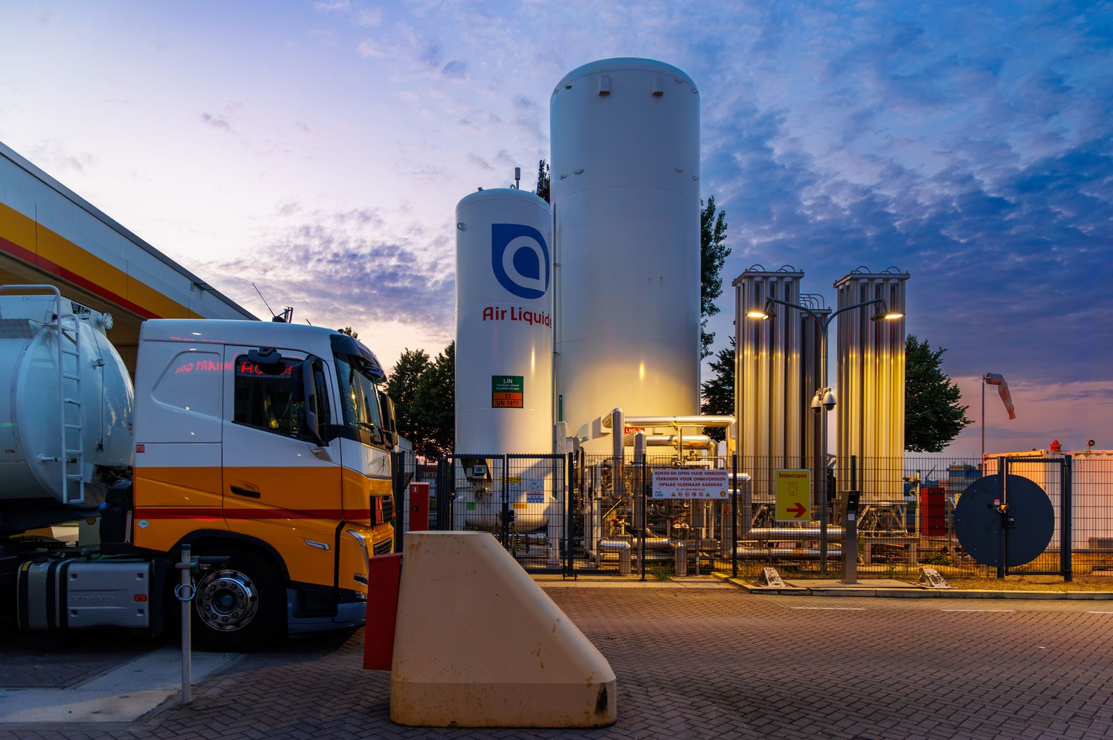 Fuel tanker truck at a filling station during golden hour, driver refueling nozzle in focus