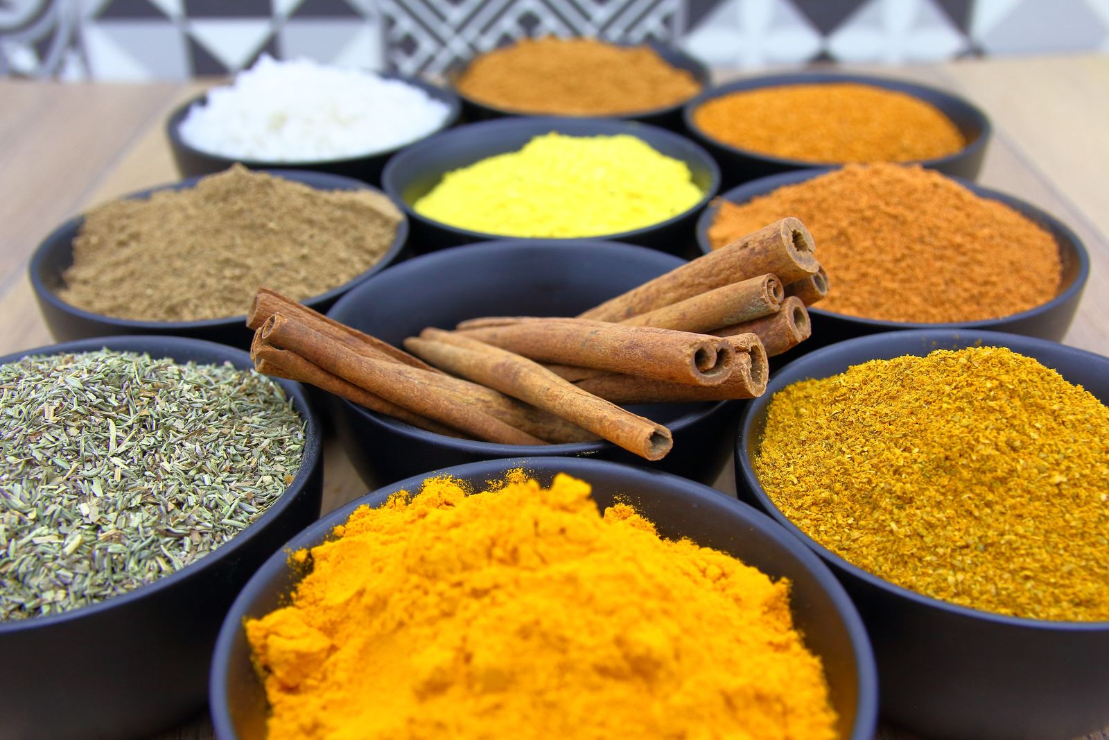 Colorful spices including chili, turmeric and cinnamon in wooden bowls on a rustic table